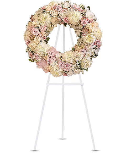 Floral wreath with pink and off white flowers on a white stand 