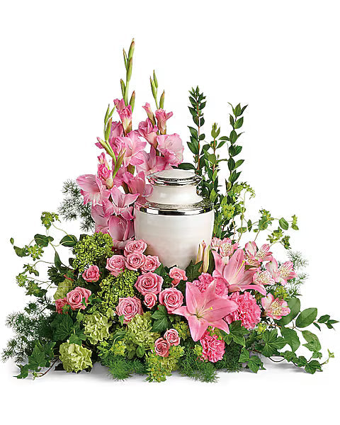 Fresh pink flowers with green leaves arranged around silver urn on white surface